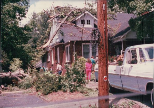 A brick house with a large limb broken onto its roof and debris in the yard