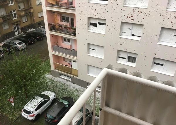 An apartment building facade covered with dark hail impact marks and cars with dented roofs below