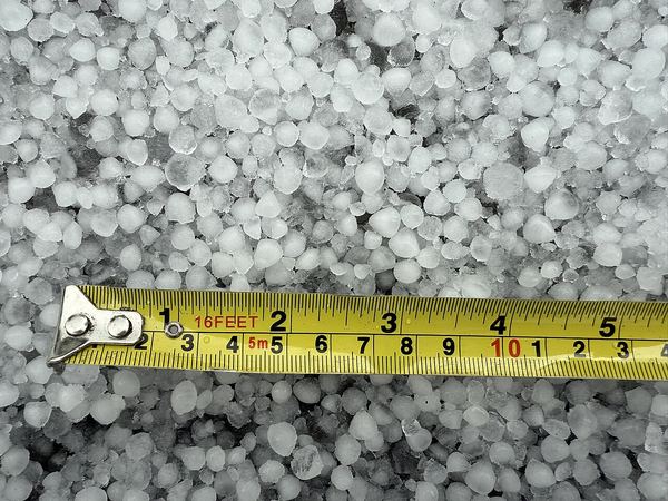 A tape measure laid across a carpet of small hailstones