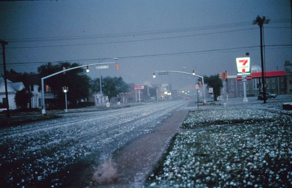 Large hailstones covering a street and grass at dusk