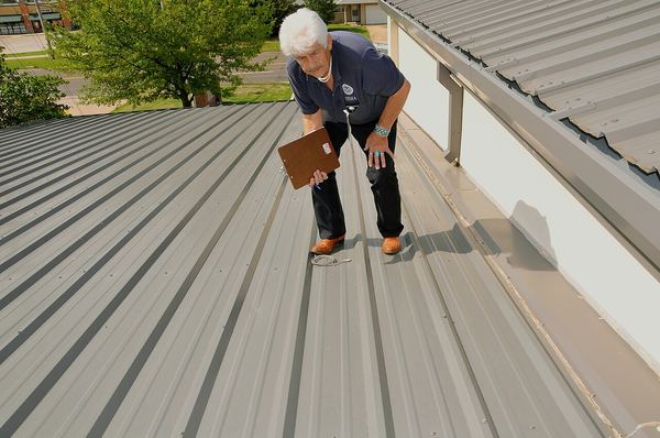 A FEMA inspector bends to look along a ribbed metal roof for hail dents after a 2010 storm in Moore, Oklahoma