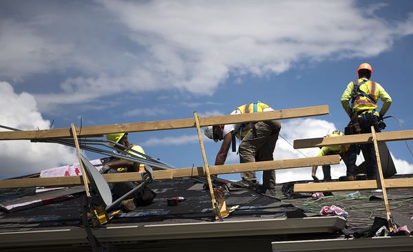 Roofing crew installing new shingles on base housing roofs damaged by a 2018 hailstorm