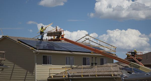Workers on a lift and roof replacing shingles on a row of two-story homes after hail