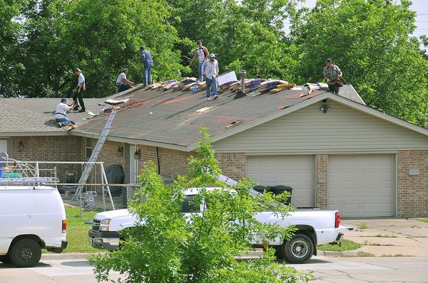 A roofing crew tearing off and replacing shingles on a single-story house