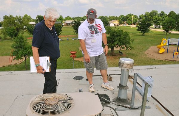 Two men inspect hail damage to a rooftop air conditioning unit and vent stacks on a flat roof