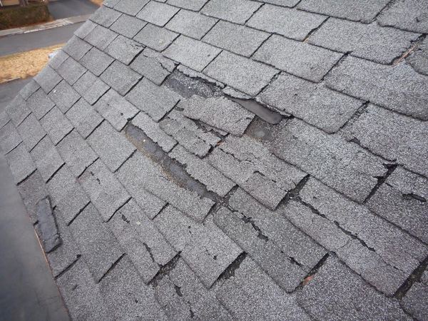 Gray shingles with lifted, misaligned courses on a steep roof