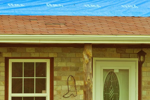 A brick house with a blue tarp covering its damaged roof